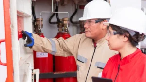 Two safety engineers reviewing a red compliance label on a commercial fire suppression cylinder system with a digital tablet.