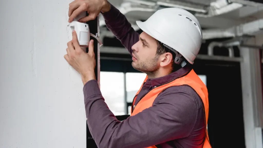 A technician installing a fire alarm on the ceiling to ensure safety and protection