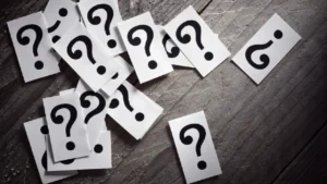 Pile of question marks on a wooden table representing confusion or seeking answers.